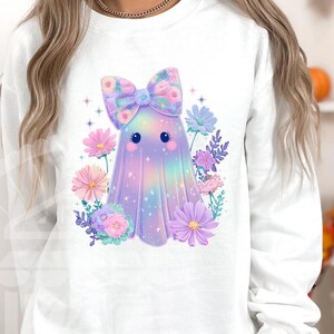 Pode incluir: Camisola branca com um personagem de fantasma fofo com um la&ccedil;o floral e rodeado por flores pastel. O fantasma tem um design colorido e iridescente. Perfeito para o Halloween ou uma est&eacute;tica caprichosa.