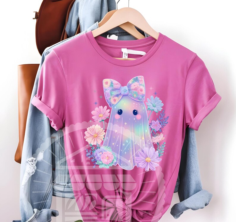 Pode incluir: Uma camiseta rosa com um desenho de fantasma de desenho animado. O fantasma tem um la&ccedil;o floral e &eacute; cercado por flores coloridas. O corpo do fantasma tem um efeito de gradiente de arco-&iacute;ris. A camiseta &eacute; de manga curta e gola redonda.