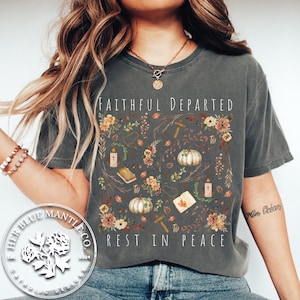 May include: Dark gray t-shirt with the words "FAITHFUL DEPARTED" and "REST IN PEACE" in white. The shirt features a floral design with pumpkins, candles, and crosses. The design is centered on the front of the shirt.