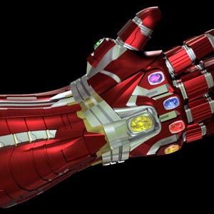 Pode incluir: Uma manopla metálica vermelha e prateada com pedras preciosas coloridas embutidas. A manopla apresenta um design segmentado com detalhes intrincados sobre um fundo preto. As pedras preciosas são de várias cores, incluindo verde, roxo, azul, amarelo e vermelho.