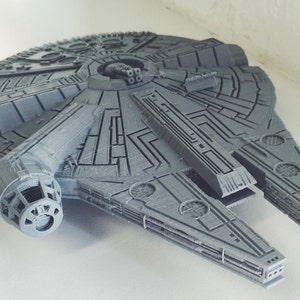 May include: A grey 3D printed model of the Millennium Falcon spaceship from Star Wars. The model is detailed with the iconic features of the ship, including the cockpit, engines, and wings.