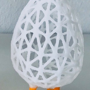 May include: A white, egg-shaped decorative object with a geometric, openwork design. The egg rests on two bright orange chicken feet. The object is likely a decorative item or Easter-themed ornament.
