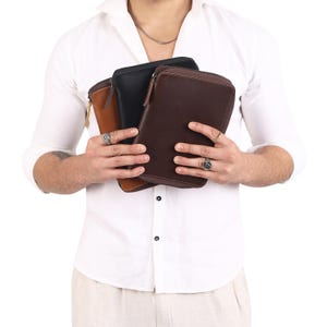 May include: Three leather wallets in brown, black, and tan with zippers. The wallets are held in the hands of a person.