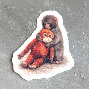 May include: A sticker featuring a gray monkey hugging an orange stuffed monkey. The sticker has a white border and is set against a gray background. The image is a detailed illustration of the two monkeys.