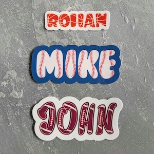 May include: Three name stickers: "ROHAN" in orange basketball design, "MIKE" in baseball design with a blue border, and "JOHN" in a maroon football design.