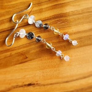 May include: A pair of silver dangle earrings featuring a selection of gemstone beads, including clear, pink, yellow, and blue. The earrings have a silver hook fastening.