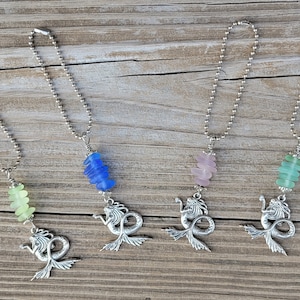May include: Four silver charm necklaces with mermaid charms and different colored sea glass beads. The beads are light green, blue, pink, and green.