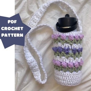 May include: White crocheted water bottle holder with a purple, green, and white pattern. The holder is attached to a white crocheted strap.