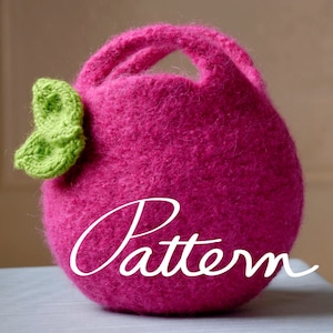 Pode incluir: Uma bolsa de mão de malha rosa com um laço de malha verde. A bolsa tem uma alça e a palavra "Pattern" está escrita na frente.