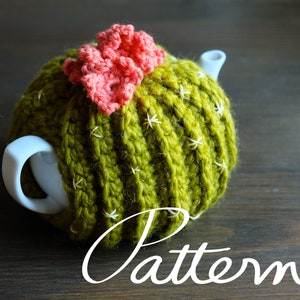 May include: Green crocheted teapot cosy shaped like a cactus with a pink crocheted flower on top.