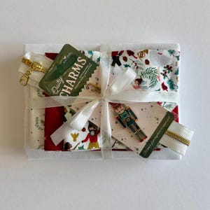 Può includere: Un pacchetto di tessuti legato con un nastro bianco, completo di un ciondolo in metallo a tema schiaccianoci e un tiralampo. Il tessuto presenta motivi natalizi con schiaccianoci, ballerini e vegetazione. Un'etichetta riporta Quilty Charms.