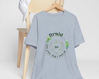 Puede incluir: Camiseta azul claro con un gráfico verde y marrón de un dado de veinte caras con la palabra "Druid" encima y el texto "Tell your dog I said hi" alrededor del dado.