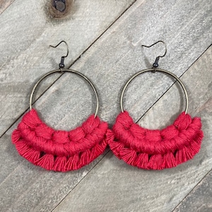 May include: A pair of red crocheted hoop earrings with a fringe detail. The earrings are made with a thick, red yarn and have a simple, minimalist design.