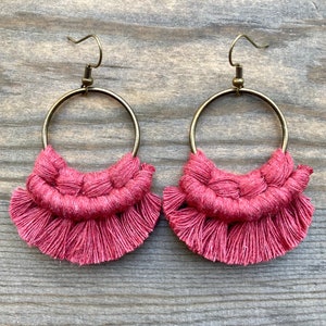 May include: A pair of pink macrame earrings with gold hoops. The earrings have a fringe detail and are handmade.