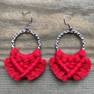 May include: A pair of red and silver hoop earrings with a crocheted design. The earrings have a silver hoop with a textured finish and a red crocheted tassel hanging from the bottom.