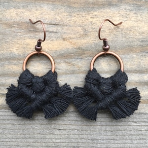 May include: Black macrame earrings with copper hoops and hooks. The earrings feature a knotted design with fringe details.