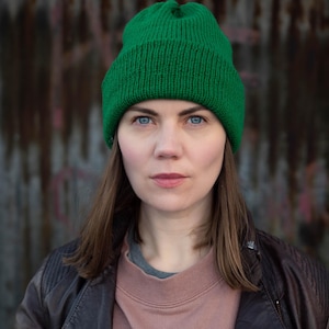 May include: A vibrant green knit beanie with a ribbed texture and a folded cuff. The hat is constructed from a solid-colored yarn and features a classic pull-on design that covers the crown of the head, providing a simple and functional head covering.