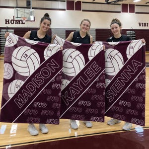 Puede incluir: Tres mantas de forro polar granate y blanco con gr&aacute;ficos de voleibol, los nombres MADISON, KAYLEE y SIENNA, y los n&uacute;meros 12, 7 y 22. Las mantas muestran un patr&oacute;n repetitivo de peque&ntilde;os balones de voleibol, corazones y signos de paz.