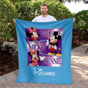 May include: A light blue blanket featuring Mickey and Minnie Mouse. The blanket has a central panel with images of Mickey and Minnie, along with the names "Minnie" and "Mickey". The name "Richard" is written in white script at the bottom.