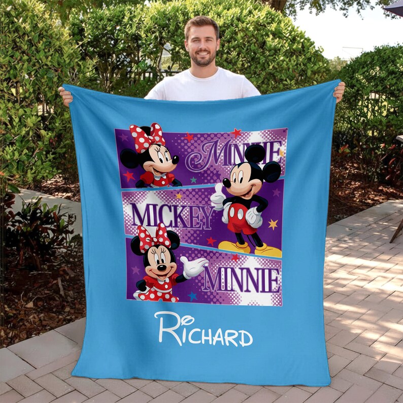May include: A light blue blanket featuring Mickey and Minnie Mouse. The blanket has a central panel with images of Mickey and Minnie, along with the names "Minnie" and "Mickey". The name "Richard" is written in white script at the bottom.