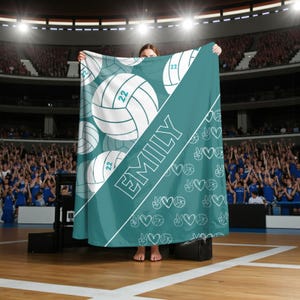 Puede incluir: Una manta de color verde azulado con un patr&oacute;n de balones de voleibol blancos con el n&uacute;mero 22, una franja diagonal blanca con el nombre EMILY en letras may&uacute;sculas blancas y un patr&oacute;n repetido de peque&ntilde;os balones, corazones y signos de paz.