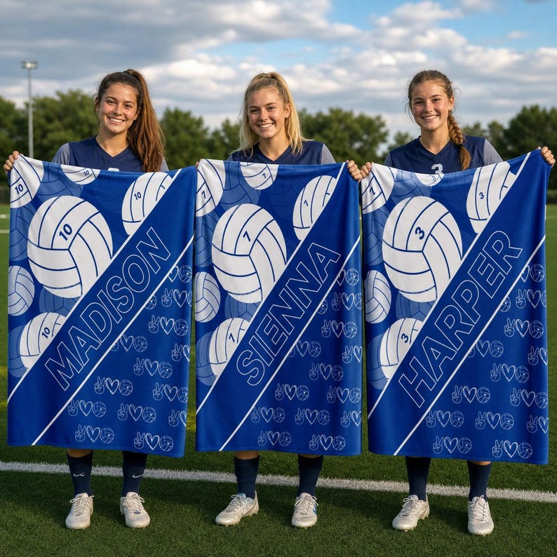 Puede incluir: Tres mantas rectangulares azules con una franja diagonal blanca, gr&aacute;ficos de voleibol con n&uacute;meros y peque&ntilde;os iconos de corazones y signos de paz. Cada manta est&aacute; personalizada con los nombres Madison, Sienna o Harper en texto blanco.