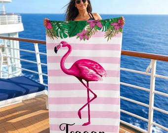 May include: A rectangular beach towel featuring a pink and white horizontal striped pattern. The towel displays a large, vibrant pink flamingo in the center and a border of green tropical leaves and pink flowers at the top. The name Teagan is printed in black script at the bottom.