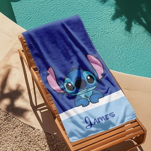 May include: A blue beach towel featuring a cartoon character with large ears and big eyes. The towel has a white and light blue stripe at the bottom with the name "James" in script.