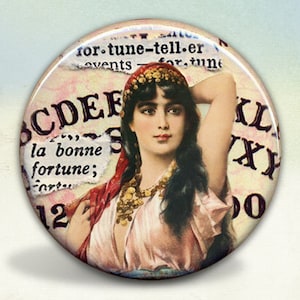 May include: A vintage-style button featuring a woman with dark hair and a red headscarf. The background is a light pink with a white paper overlay that reads "la bonne fortune". The button also features a black and white alphabet.