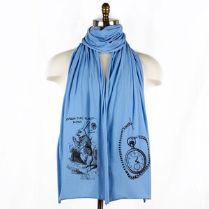 May include: A light blue scarf with a black and white illustration of the White Rabbit from Alice in Wonderland and a pocket watch with a chain. The text on the scarf reads "Down the Rabbit-Hole, Chapter I."