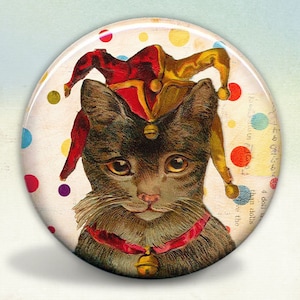 May include: A black cat wearing a red and gold jester hat with bells. The cat is wearing a red ribbon around its neck with a bell. The background is a white and colorful polka dot pattern.