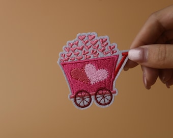 Un carrito rosa con varios corazones rosas, parche para planchar, parche bordado, aplique, etiquetas para planchar en la ropa.
