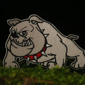 Könnte beinhalten: Ein gestickter Bulldoggen-Patch in Grau mit einem roten Halsband und schwarzen Stacheln. Der Bulldogge knurrt mit sichtbaren Zähnen.