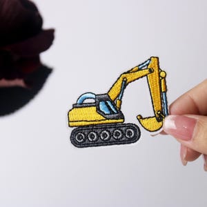 Puede incluir: Parche bordado amarillo de una excavadora con una oruga negra y detalles azules.