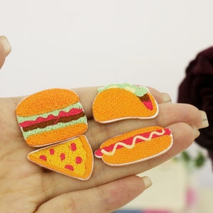 Pode incluir: Quatro patches bordados para passar a ferro que representam diferentes alimentos: um hambúrguer, um taco, um cachorro-quente e uma fatia de pizza. Os patches são amarelos, laranja, vermelhos e verdes.