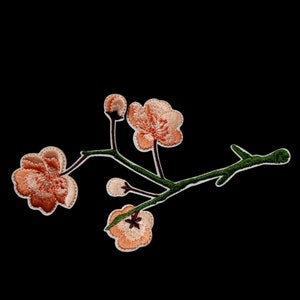 May include: A delicate embroidered patch featuring a branch of pink cherry blossoms with green leaves. The patch is perfect for adding a touch of floral charm to clothing, bags, or other crafts.