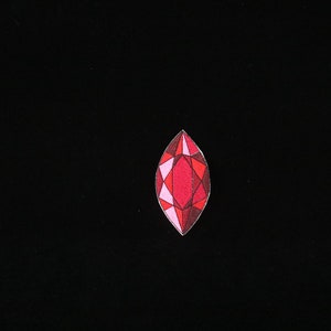 May include: A red, pink, and white gemstone with a faceted design.