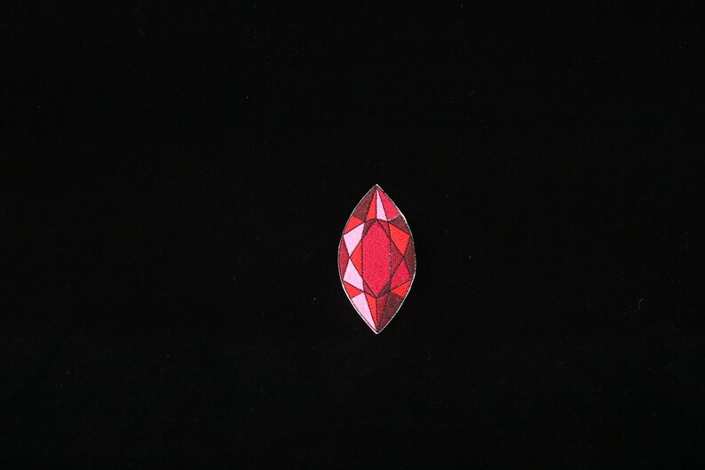 May include: A red, pink, and white gemstone with a faceted design.