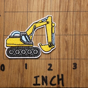 Pu&ograve; includere: Toppa ricamata gialla da stirare con un escavatore con cingoli neri e una cabina blu. La toppa &egrave; larga circa 5 cm.