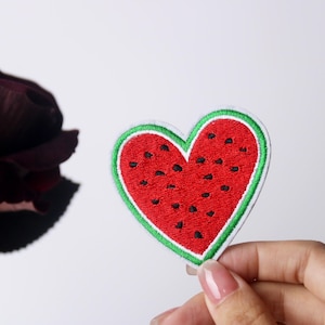 May include: A red and green embroidered watermelon heart patch. The patch is shaped like a heart and has a watermelon design with black seeds.