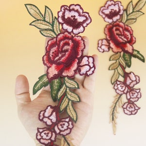 May include: Two embroidered floral appliques with pink and red roses and green leaves. The appliques are on a beige background.