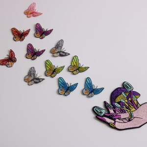 May include: A hand with colorful mushrooms growing from it, with a variety of colorful butterflies flying away from the hand.