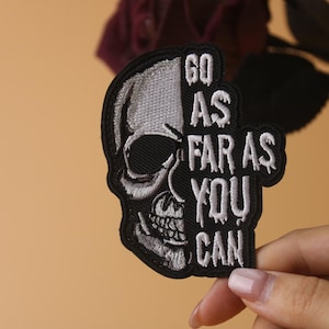May include: Black and white embroidered patch with a skull design and the text "Go as far as you can".