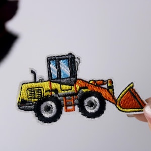 Może przedstawiać: Żółto-pomarańczowa haftowana naszywka z ładowarką czołową.