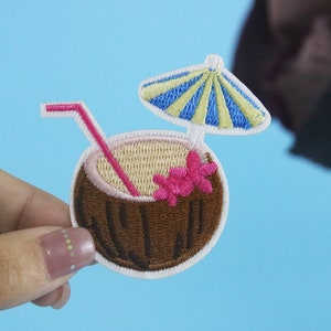 May include: Embroidered patch of a brown coconut with a pink flower, a yellow and blue striped umbrella, and a pink straw.