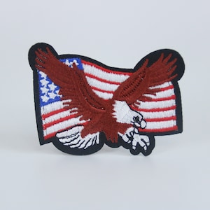 May include: An embroidered patch featuring a red bald eagle flying in front of a waving American flag. The flag is red, white, and blue with white stars on a blue field.