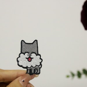 May include: A gray embroidered iron-on patch of a cartoon dog with a fluffy white beard and a red tongue sticking out.