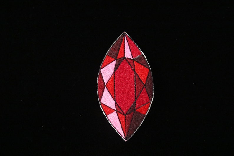 May include: A red and pink gemstone with a faceted design. The gemstone is embroidered on a black fabric.