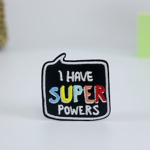Può includere: Toppa ricamata in bianco e nero con un fumetto. Il testo all'interno del fumetto recita "I have super powers" con la parola "super" in colori arcobaleno.