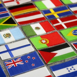 Może przedstawiać: Kolekcja haftowanych naszywek z flagami różnych krajów. Flagi są ułożone w rzędach na szarej powierzchni.